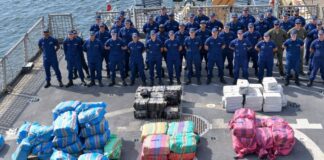 US Coast Guard crew poses behind bales of drugs seized in the Caribbean and Eastern Pacific.