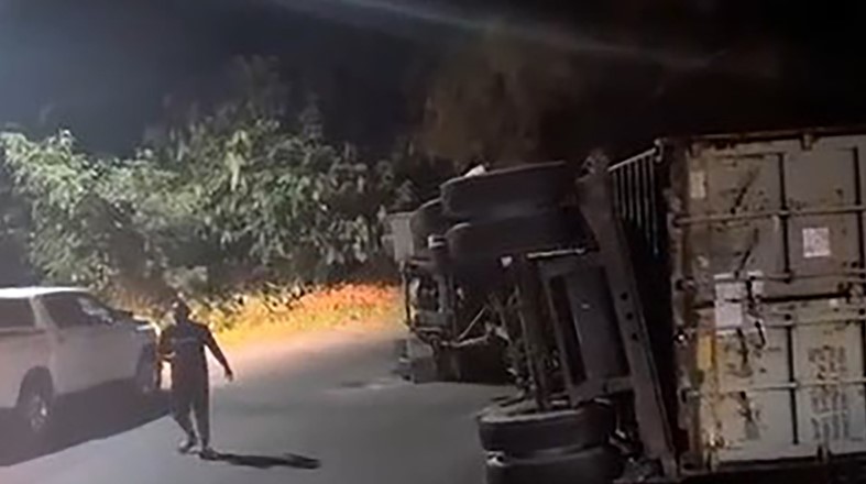 Man stands next to overturned container truck.