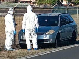 Investigators in protective white suits stand in front of vehicle in which the body of a male was found at Vigie, Castries.