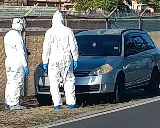 Investigators in protective white suits stand in front of vehicle in which the body of a male was found at Vigie, Castries.