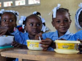 Haitian girls in school uniform eating a meal at a table.