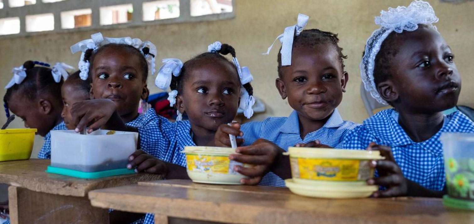 Haitian girls in school uniform eating a meal at a table.