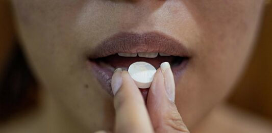 Woman puts white prescription tablet to her mouth.