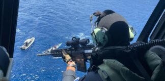Gunner in helicopter trains weapon on vessels in the water below.