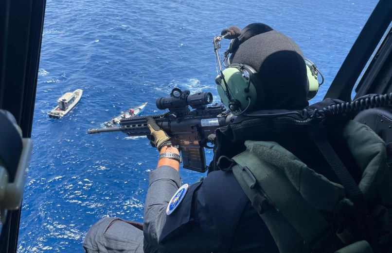 Gunner in helicopter trains weapon on vessels in the water below.