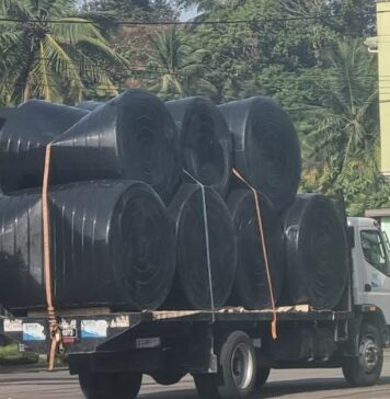 Truck carrying black plastic water tanks.