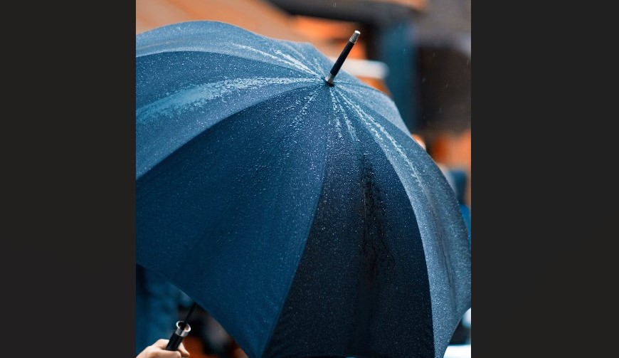 Hand holds black umbrella upon which light raindrops have fallen.