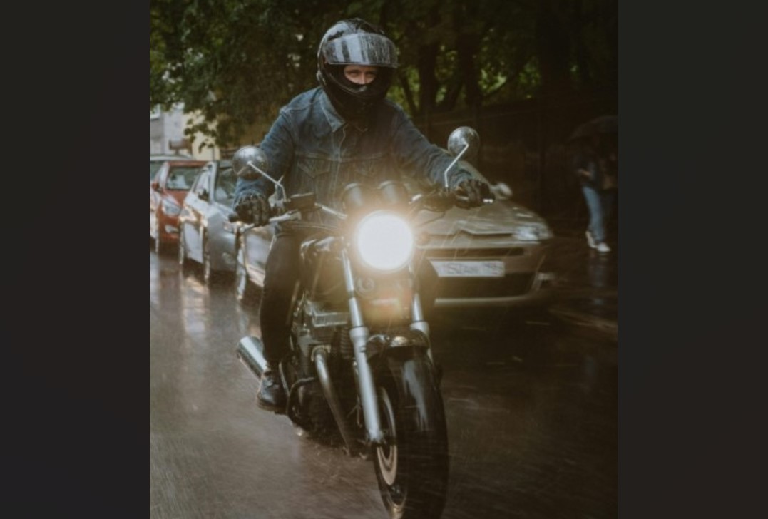 Biker with motorcycle headlights on riding at night in slight drizzle.