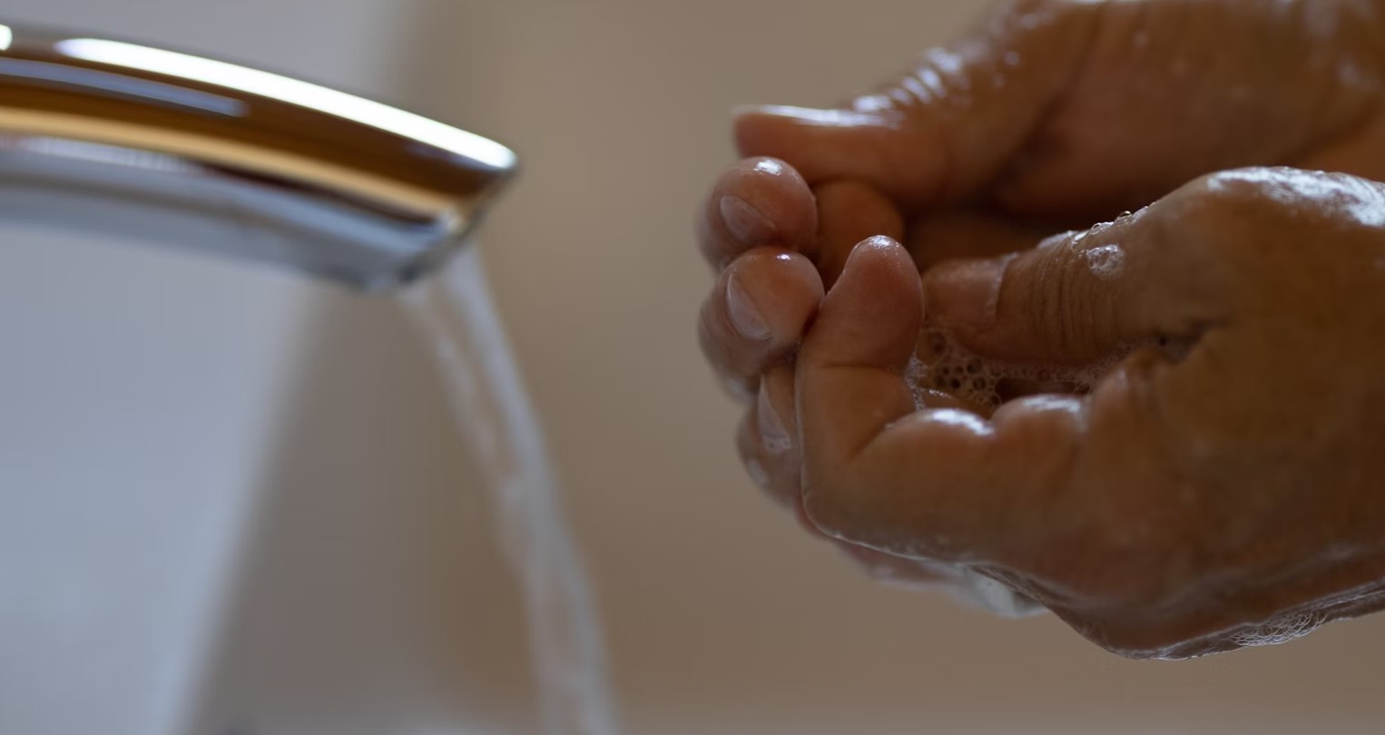 Male washing hands under faucet.