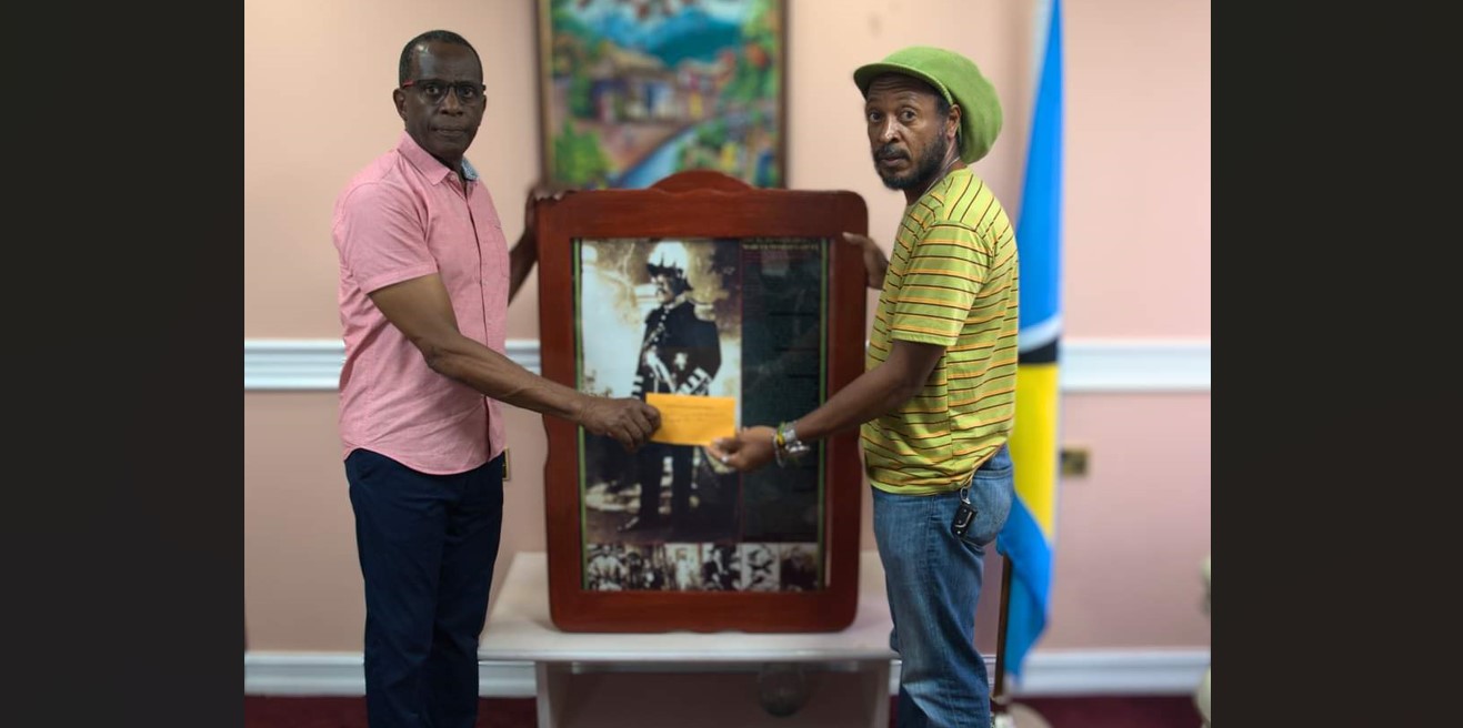 Prime Minister Philip J. Pierre presents envelope to Aaron Alexander.