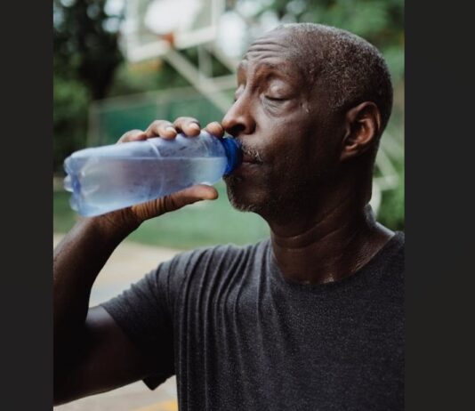 Sweating man drinks water from a bottle.