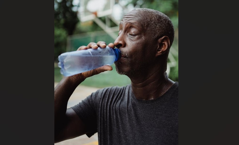 Sweating man drinks water from a bottle.